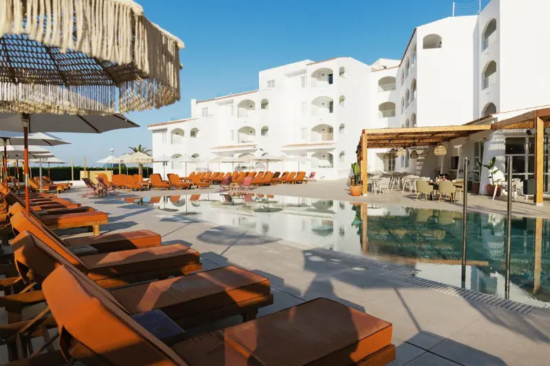 Transats orange disposés autour d'une piscine turquoise devant un bâtiment blanc.