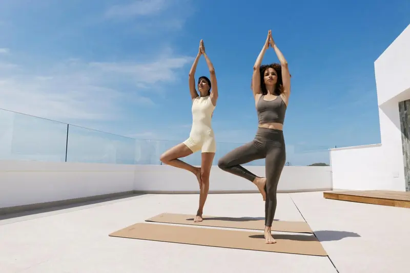 Deux femmes pratiquent le yoga sur une terrasse ensoleillée.