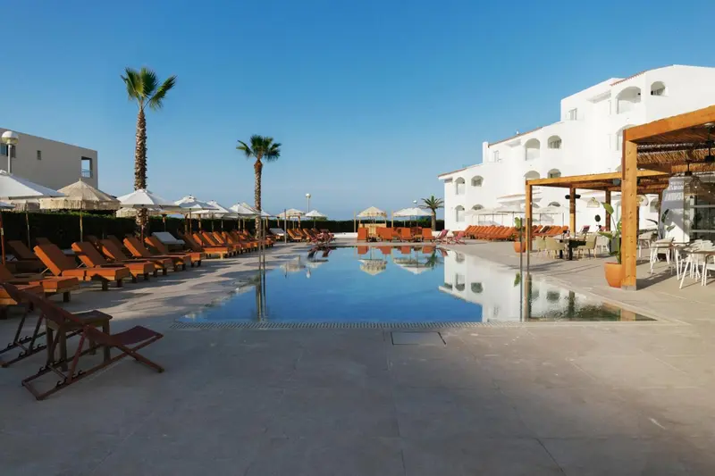 Transats et parasols bordent une piscine rectangulaire dans un espace extérieur ensoleillé.