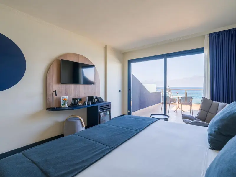 Chambre lumineuse avec un grand lit et une vue sur la mer depuis le balcon.