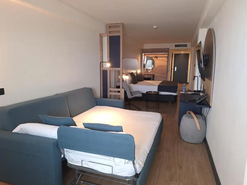 Une chambre lumineuse avec un canapé convertible et un grand lit.