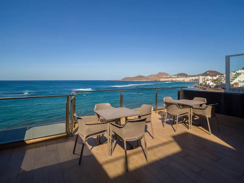 Terrasse avec tables et chaises donnant sur la mer et le littoral.