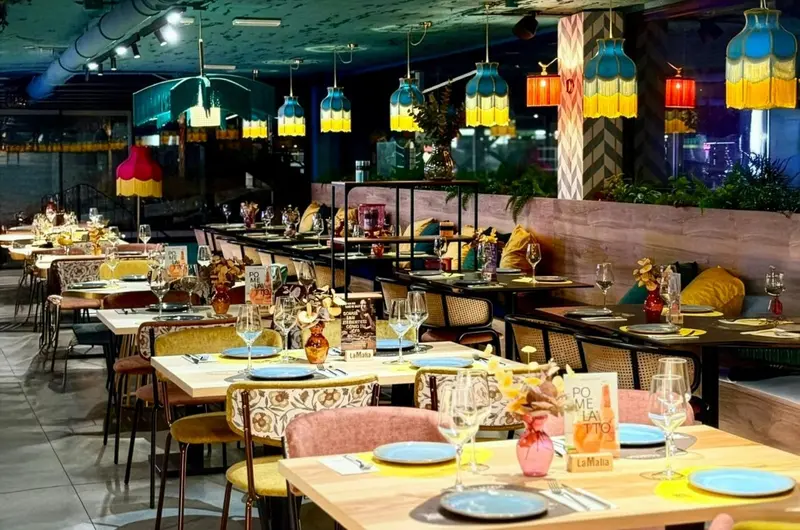Une salle de restaurant lumineuse avec des tables dressées et des suspensions colorées.