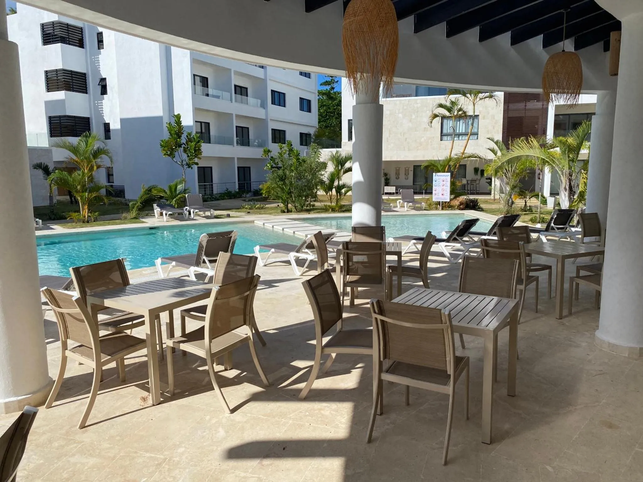 Terrasse avec tables et chaises près d'une piscine ensoleillée.
