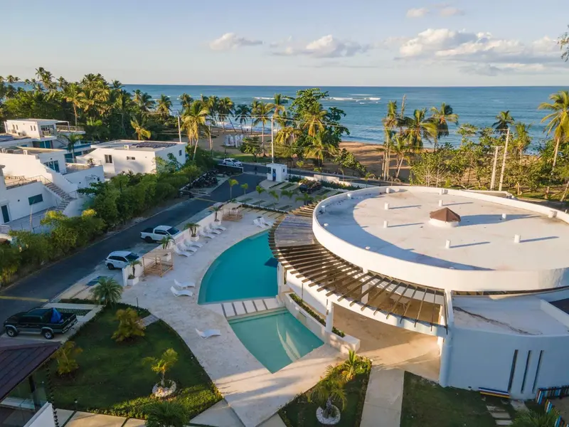 Vue aérienne d'un complexe hôtelier blanc avec une piscine et une végétation luxuriante.