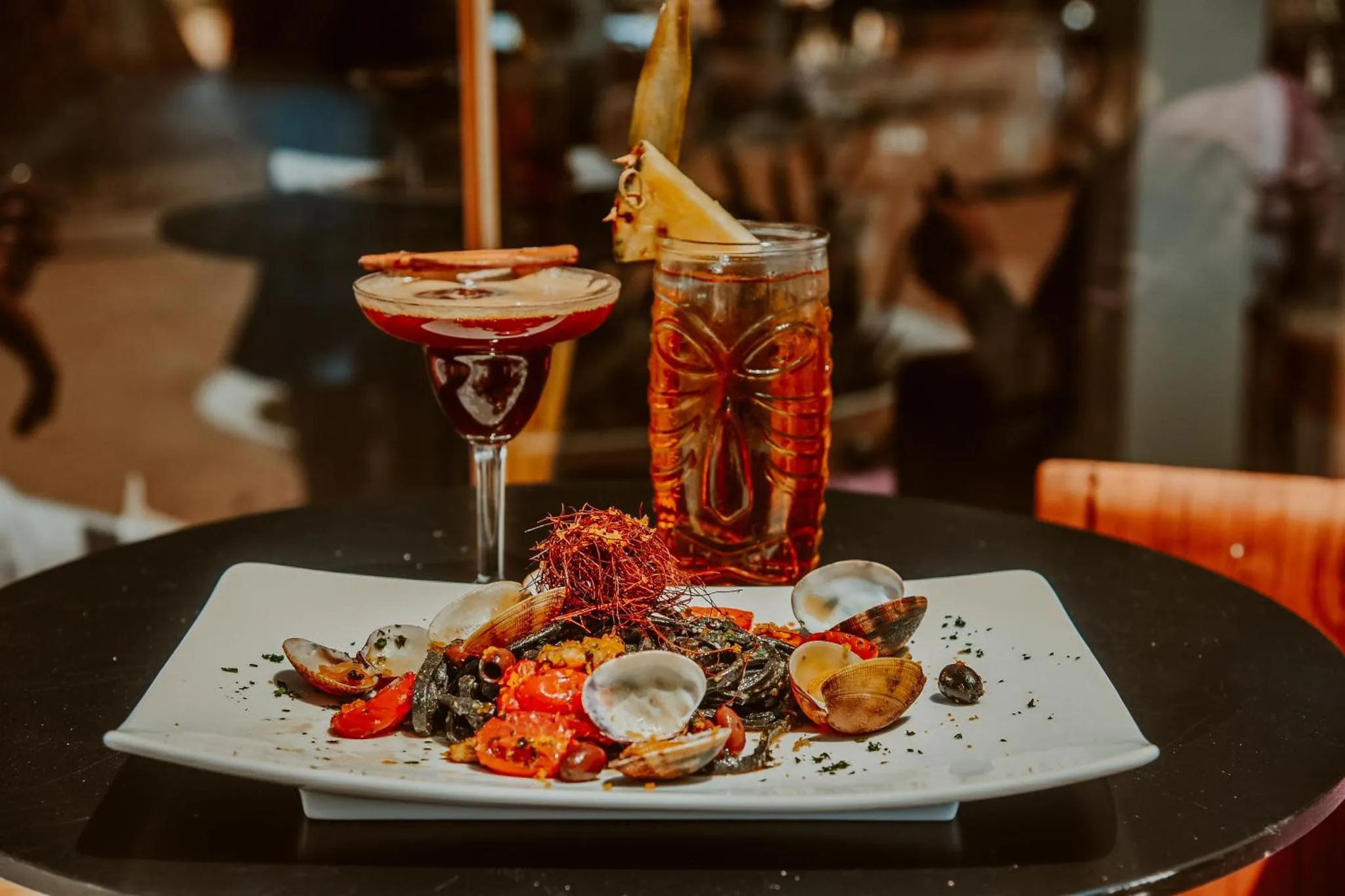 Une table présente des cocktails colorés et une assiette de fruits de mer.