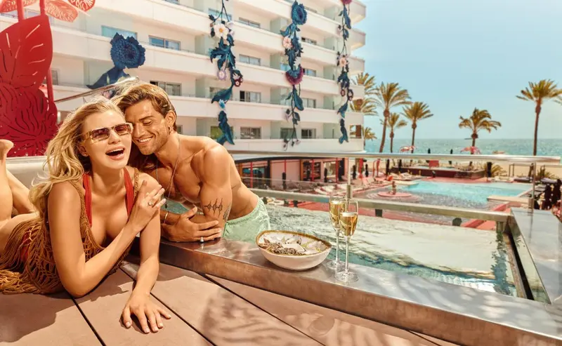 Un couple souriant se détend au bord d'une piscine avec des boissons.