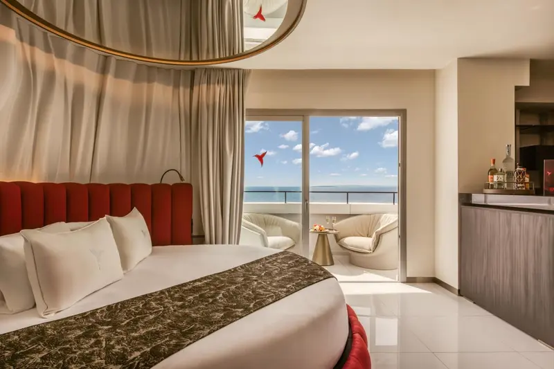 Une chambre lumineuse avec un grand lit et un balcon donnant sur la mer.