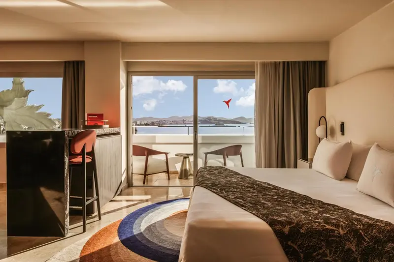 Chambre avec un grand lit et une vue sur la mer depuis une baie vitrée.