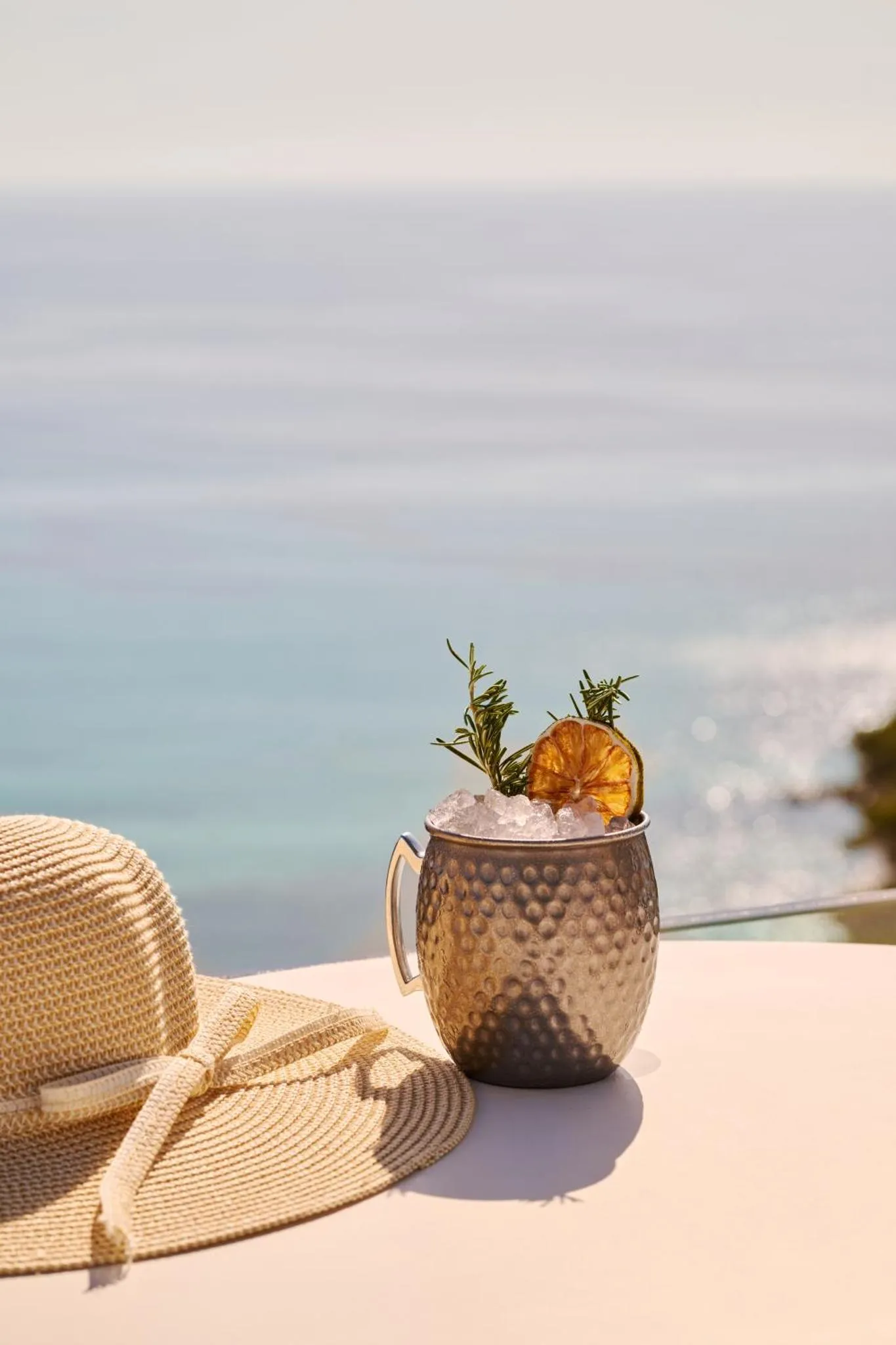 Un cocktail rafraîchissant et un chapeau de paille reposent sur une table face à la mer.