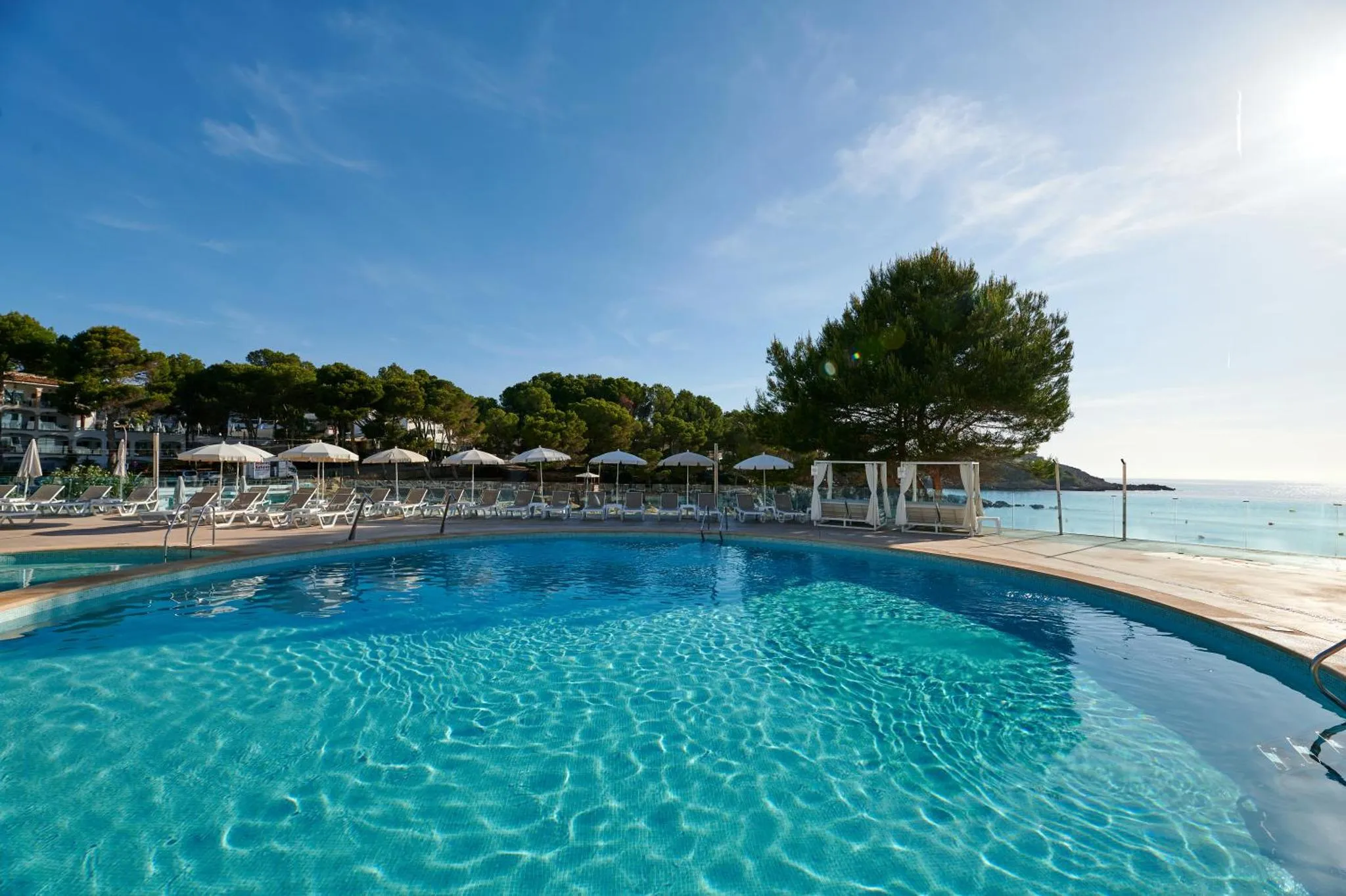 Piscine bleue bordée d'une terrasse avec transats et parasols, vue sur la mer.