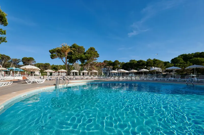 Piscine rectangulaire bordée de transats sous des parasols, dans un cadre verdoyant.