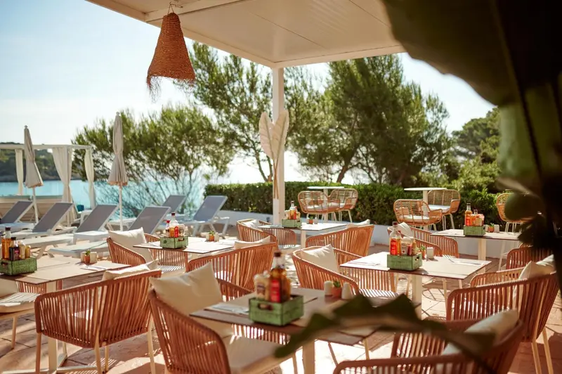 Terrasse ombragée avec tables et chaises près de la mer.
