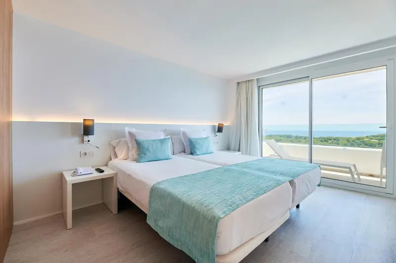 Chambre lumineuse avec lits jumeaux et vue sur la mer.