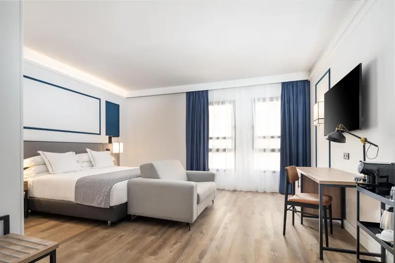 Chambre lumineuse avec un lit double, un canapé et un espace bureau.