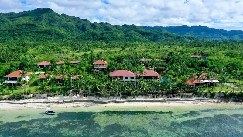 Vue aérienne d'un ensemble de bâtiments au milieu d'une végétation luxuriante, bordant une plage et une mer turquoise.