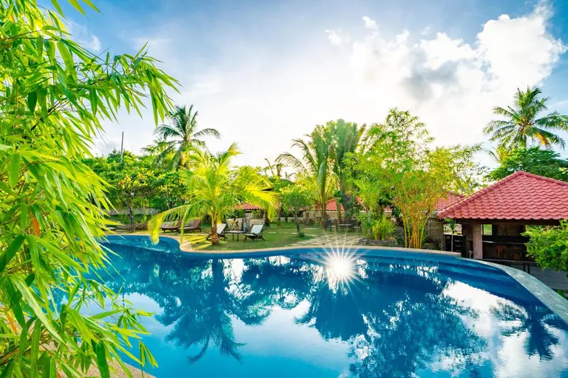 Une piscine turquoise reflète le ciel et la végétation tropicale.