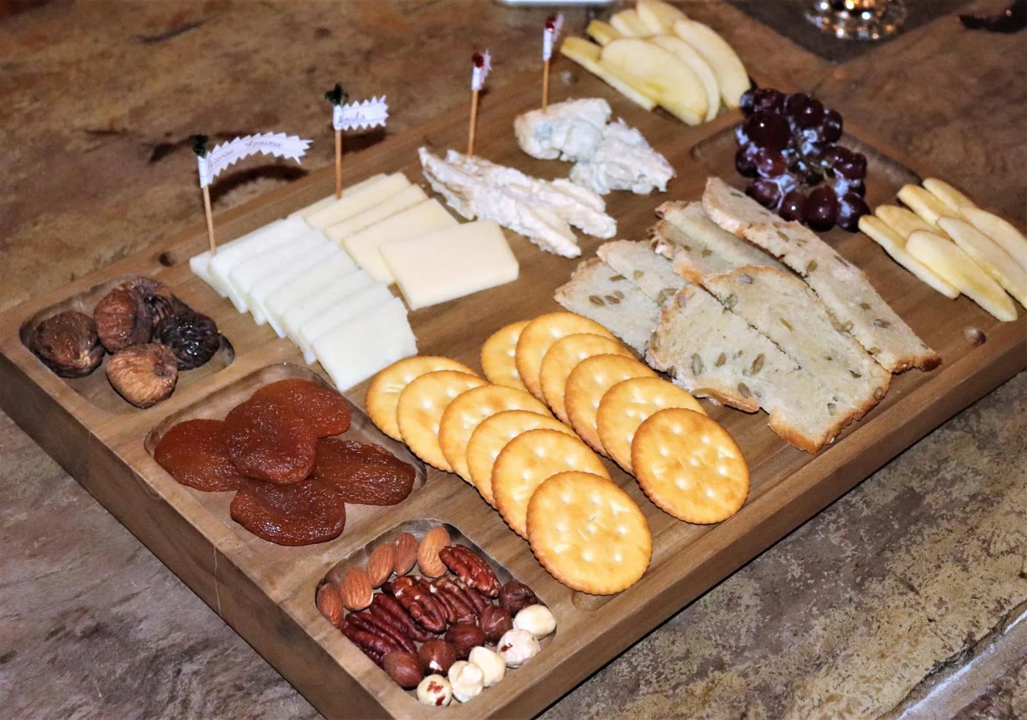Assortiment de fromages, fruits secs, crackers et noix présentés sur une planche en bois.