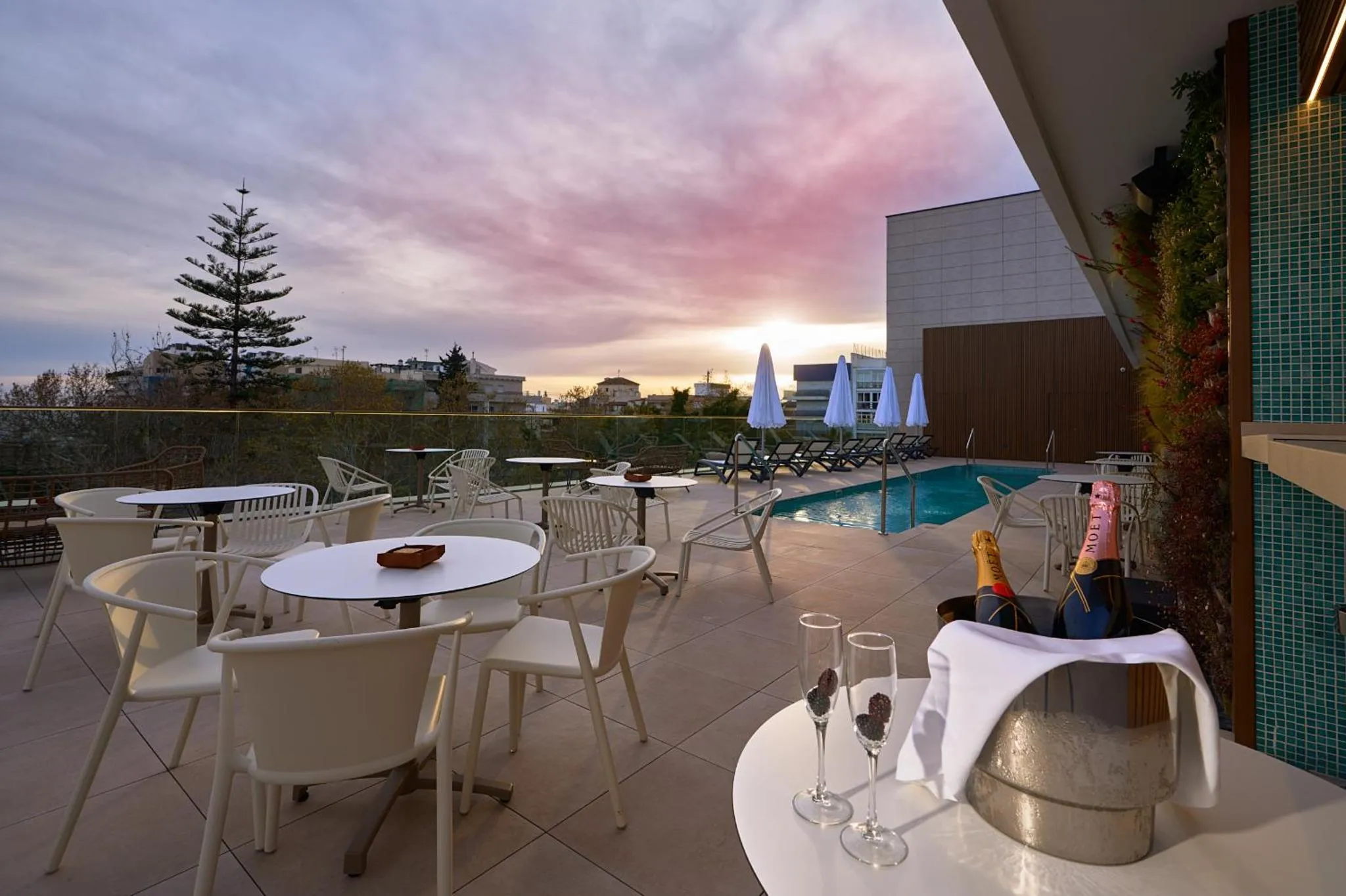 Terrasse avec tables et chaises face à une piscine et un coucher de soleil.
