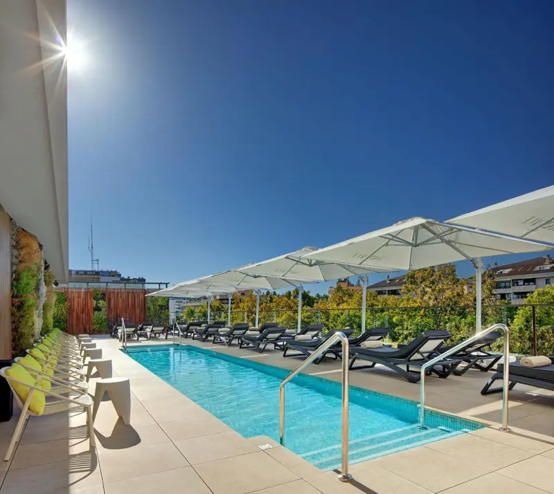 Une piscine rectangulaire bordée de transats verts sous des parasols blancs.