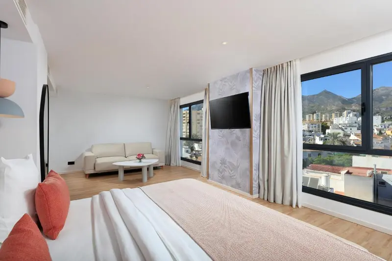 Espace de vie lumineux avec canapé et lit face à une vue sur les montagnes.