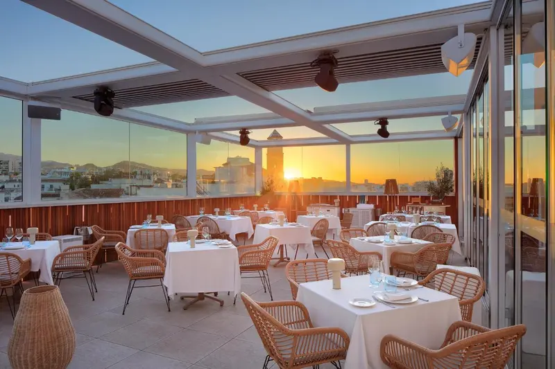 Terrasse de restaurant avec tables dressées face à un coucher de soleil sur la mer.