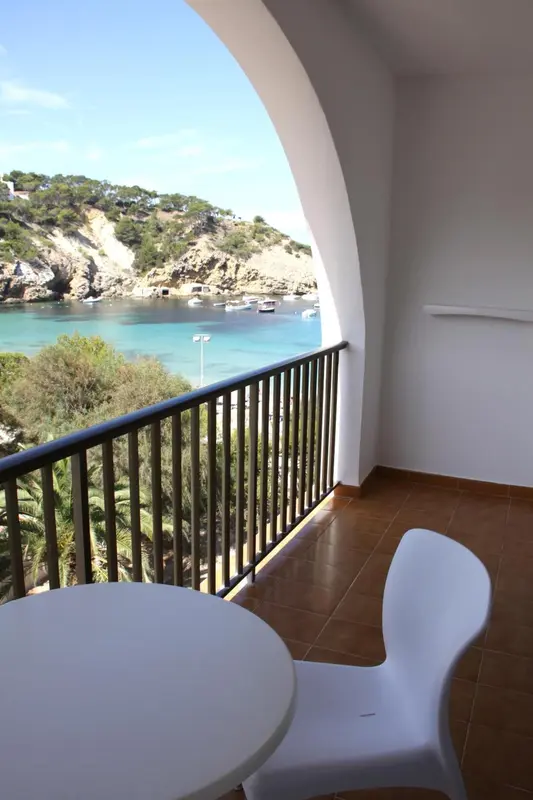 Vue sur une crique depuis un balcon avec table et chaises blanches.
