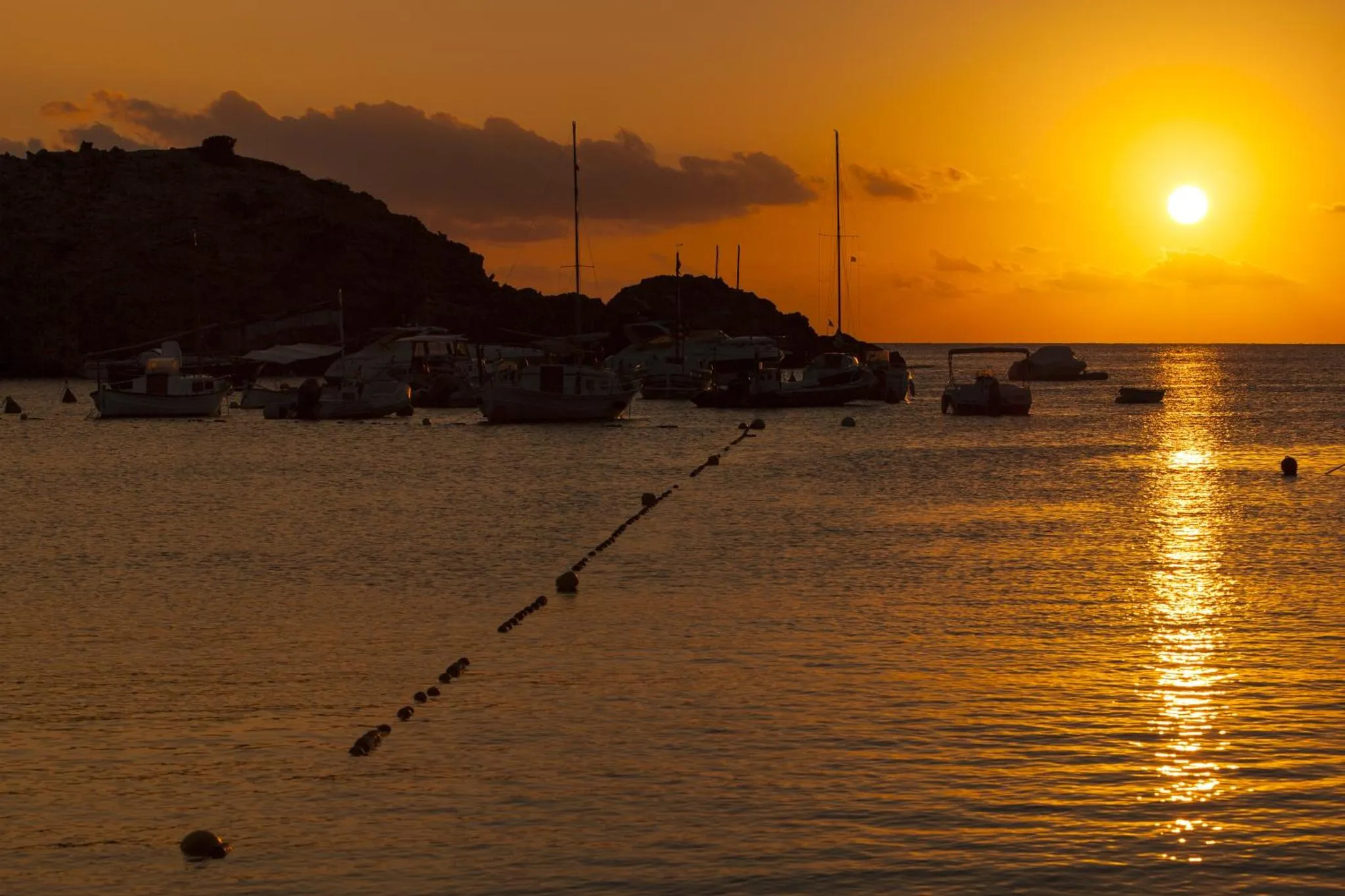 Coucher de soleil sur une baie avec des bateaux amarrés.