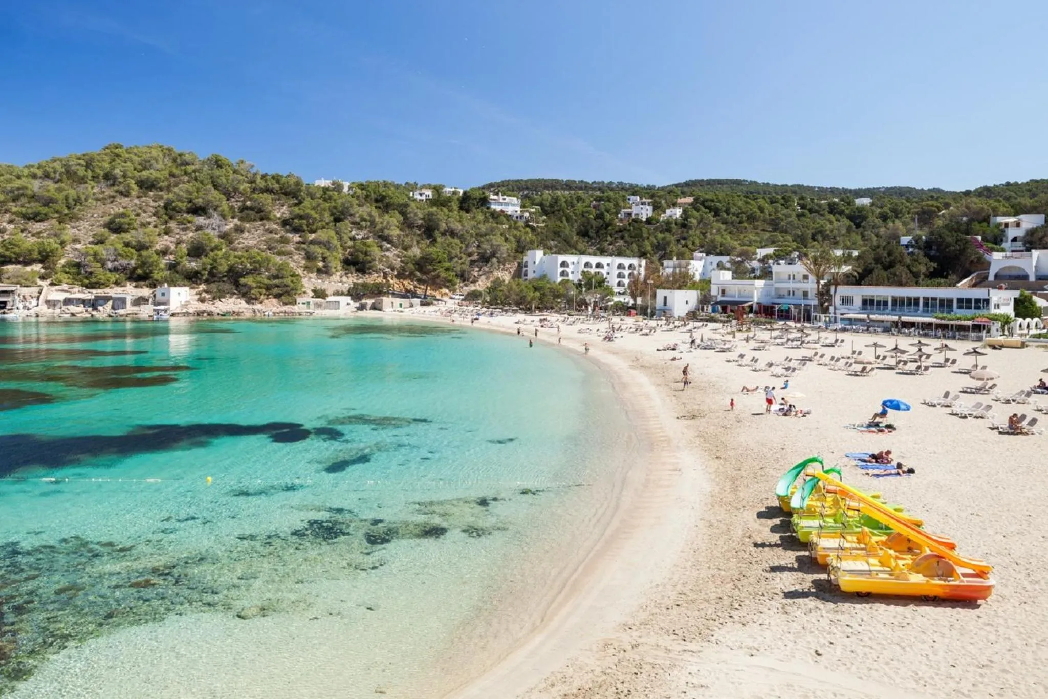 Une plage de sable fin bordée d'une eau turquoise et de quelques kayaks.