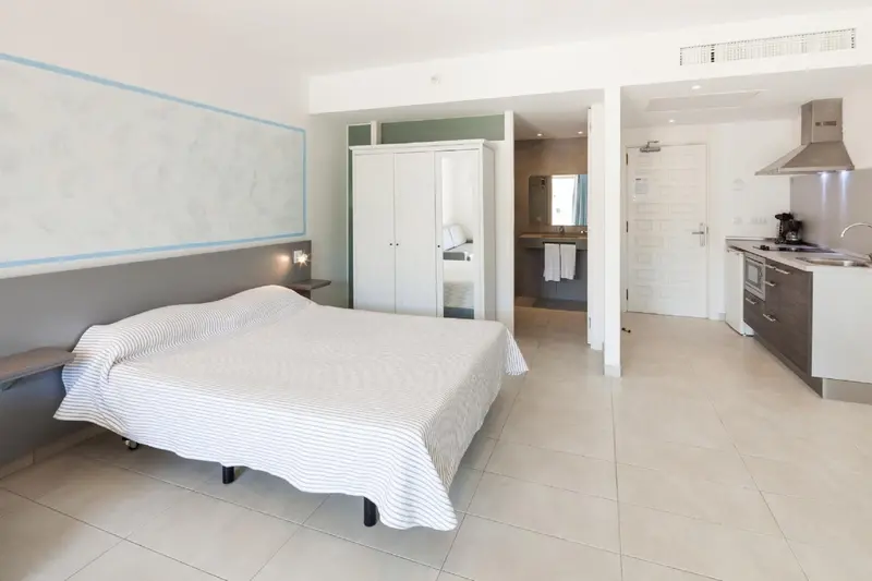 Une chambre lumineuse avec un lit fait et une kitchenette équipée.