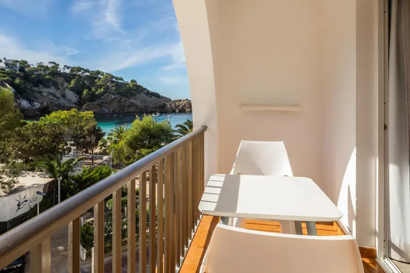 Balcon avec mobilier blanc donnant sur une crique ensoleillée.