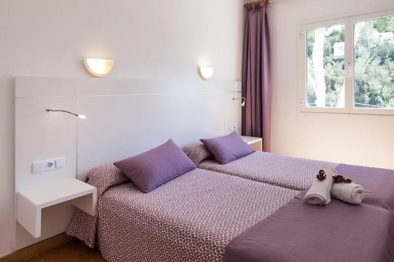 Chambre lumineuse avec deux lits simples et décoration mauve.