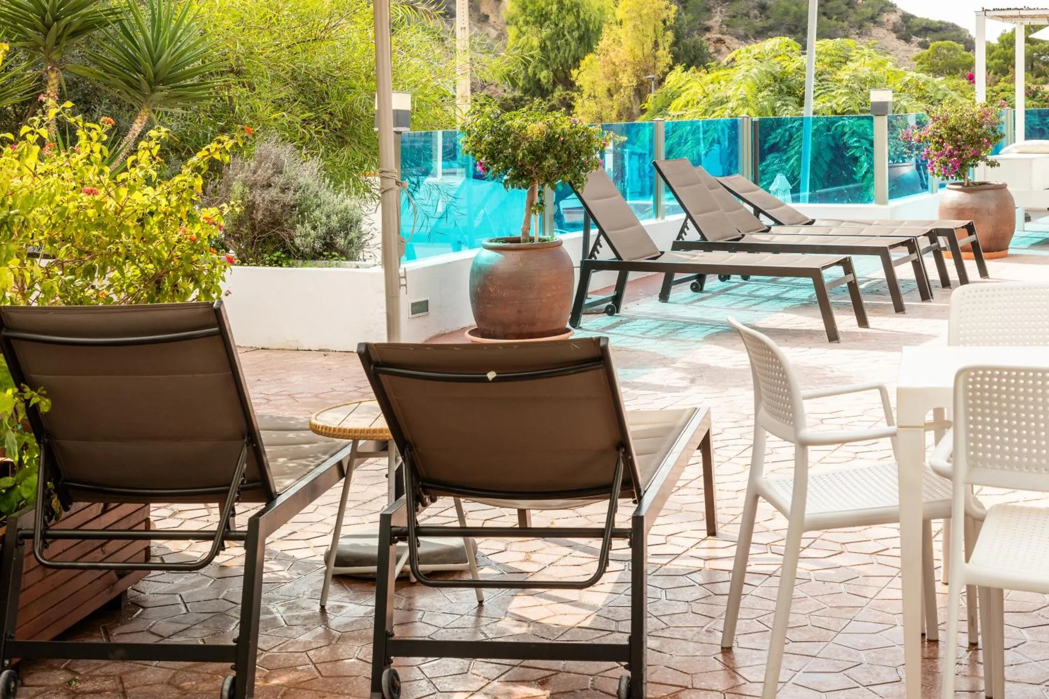 Transats et mobilier de jardin au bord d'une piscine ensoleillée.