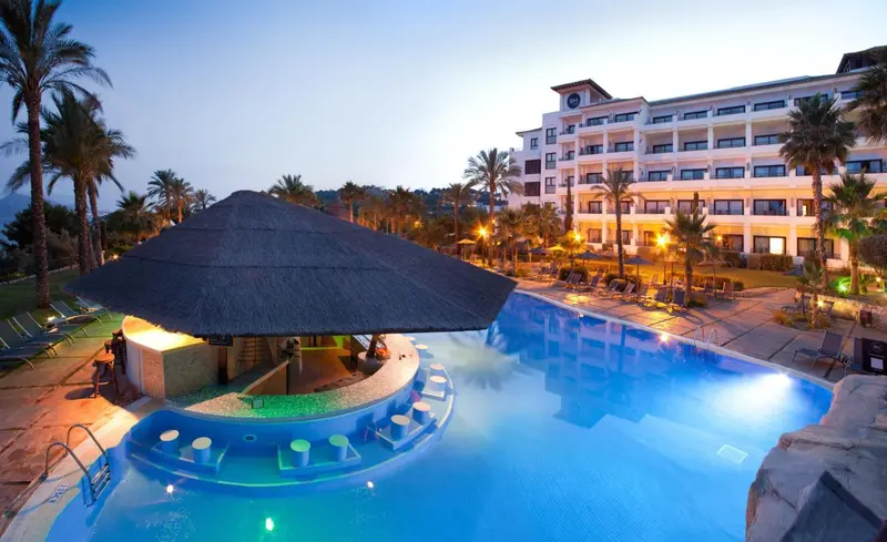 Un bar illuminé au bord d'une piscine avec un bâtiment en arrière-plan.