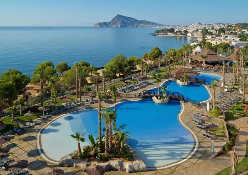Vue aérienne d'un complexe hôtelier avec piscines et végétation luxuriante face à la mer.
