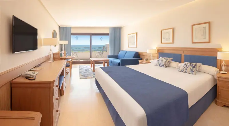 Une chambre lumineuse avec un grand lit et un canapé face à une baie vitrée.