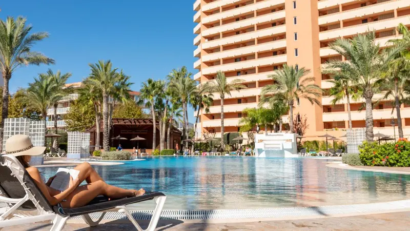 Une femme se relaxe au bord d'une piscine devant un bâtiment de plusieurs étages.