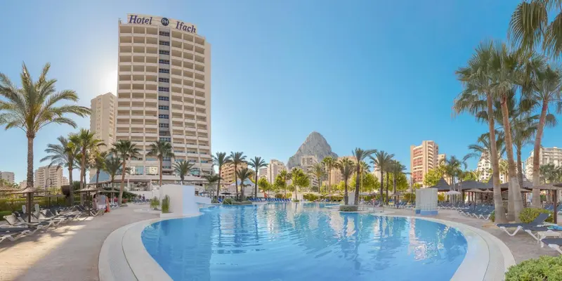 Vue d'un grand hôtel avec piscine et végétation tropicale.