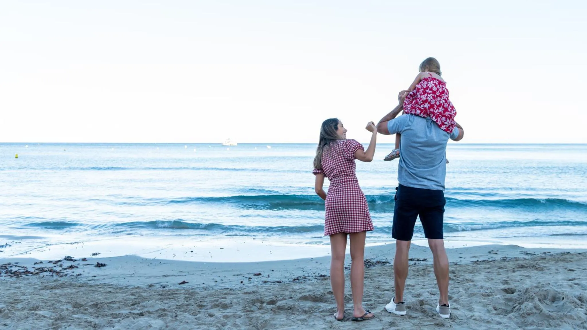 Une famille se tient sur une plage de sable fin, face à la mer.