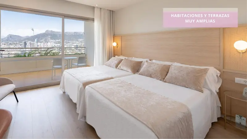 Chambre lumineuse avec grand lit et balcon offrant une vue sur la ville.