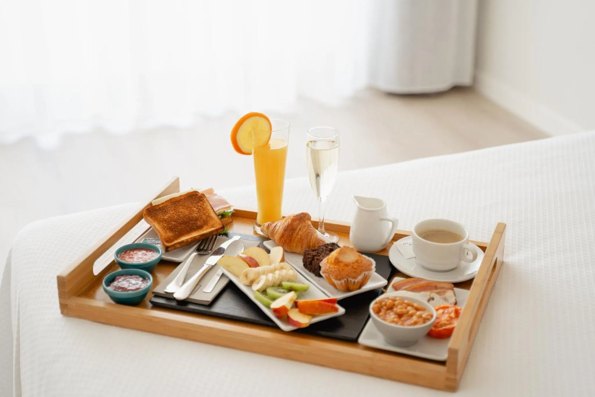 Un plateau de petit-déjeuner avec des viennoiseries, des fruits et des boissons est présenté sur un lit.