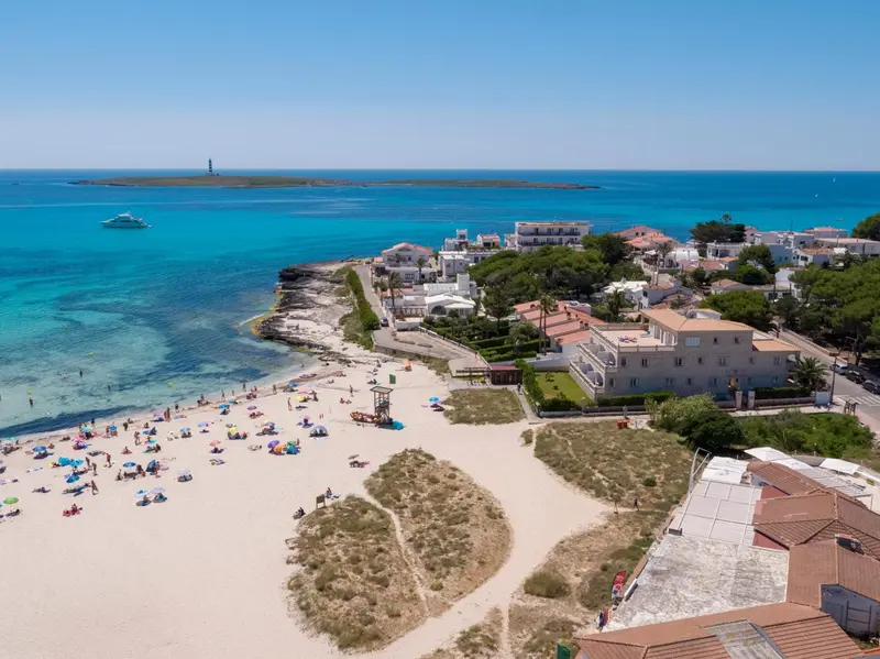Vue aérienne d'une plage de sable fin bordée d'une eau turquoise et d'une station balnéaire.