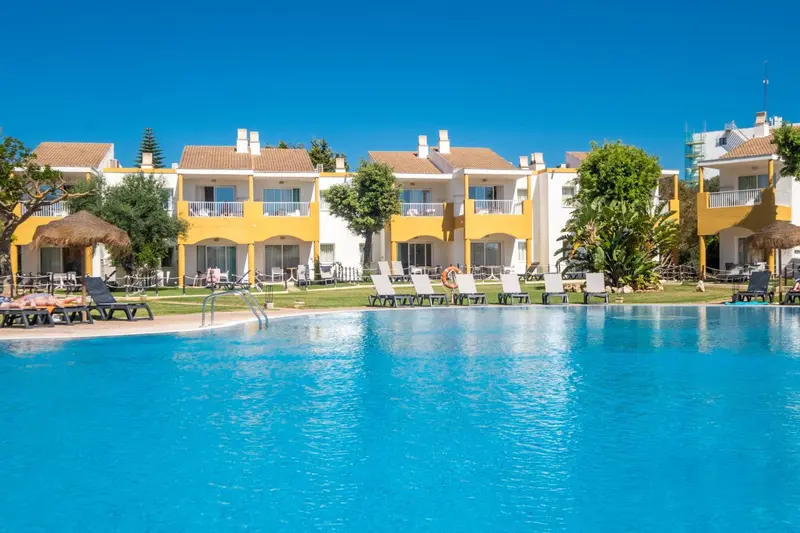 Vue d'une piscine turquoise bordée de transats devant des bâtiments aux couleurs vives.