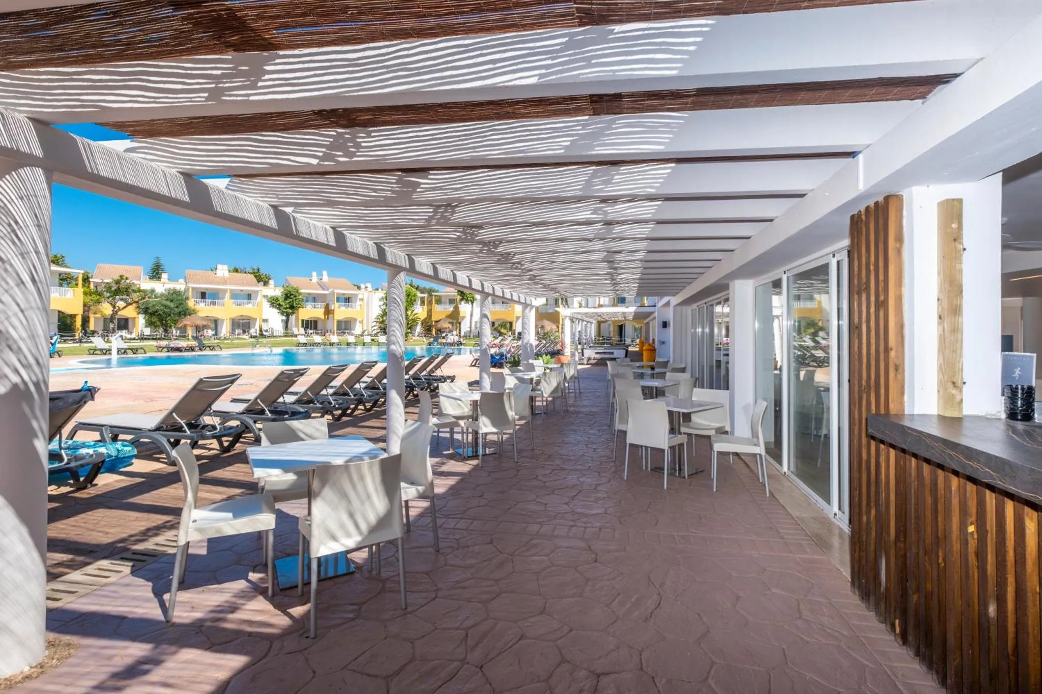 Terrasse ombragée avec tables et chaises près d'une piscine.