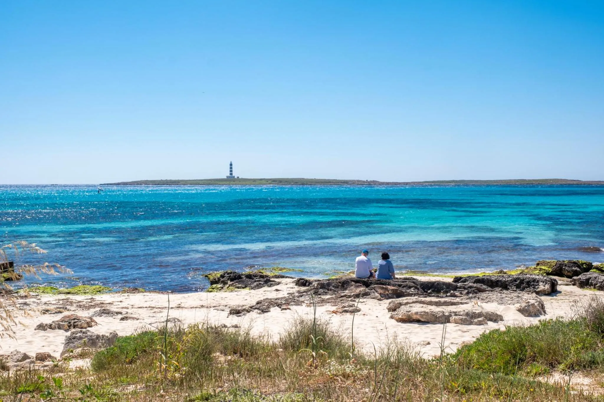 Deux personnes sont assises sur des rochers au bord de l'eau turquoise.