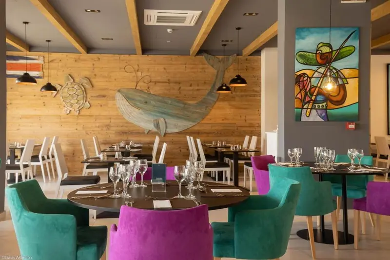 Une salle de restaurant lumineuse avec des tables dressées et des chaises colorées.