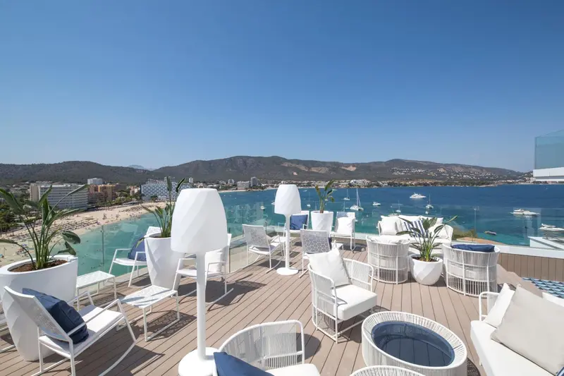 Terrasse aménagée avec mobilier blanc offrant une vue sur la mer et le littoral.