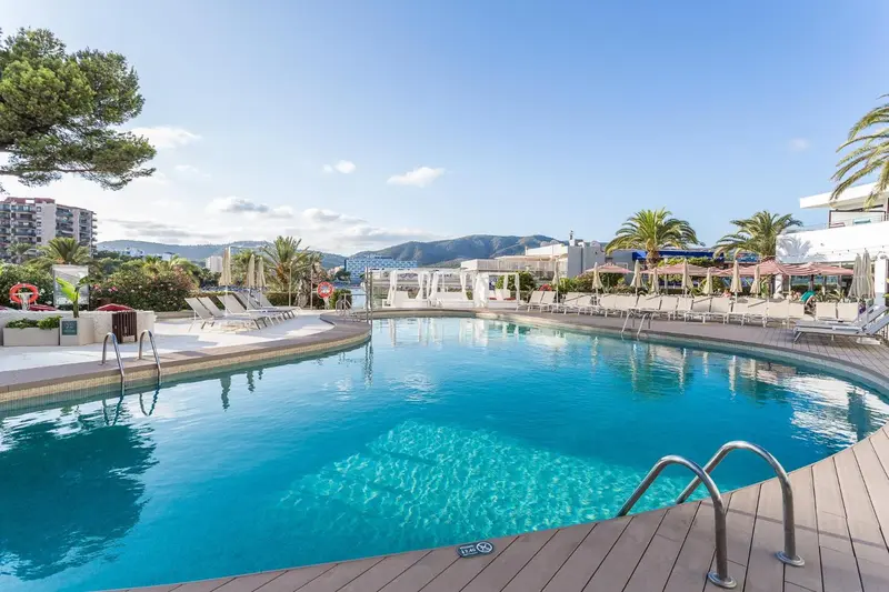 Une piscine rectangulaire bordée de chaises longues et de parasols, avec une vue sur la mer et des collines en arrière-plan.