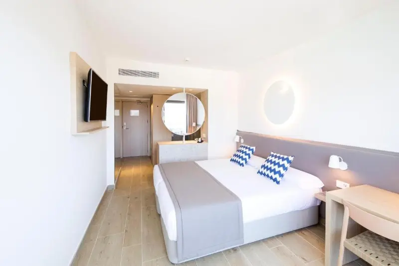 Chambre lumineuse avec un grand lit et un miroir rond au mur.