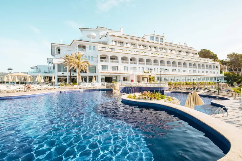 Vue d'un bâtiment blanc avec des balcons, surplombant une piscine et une plage.
